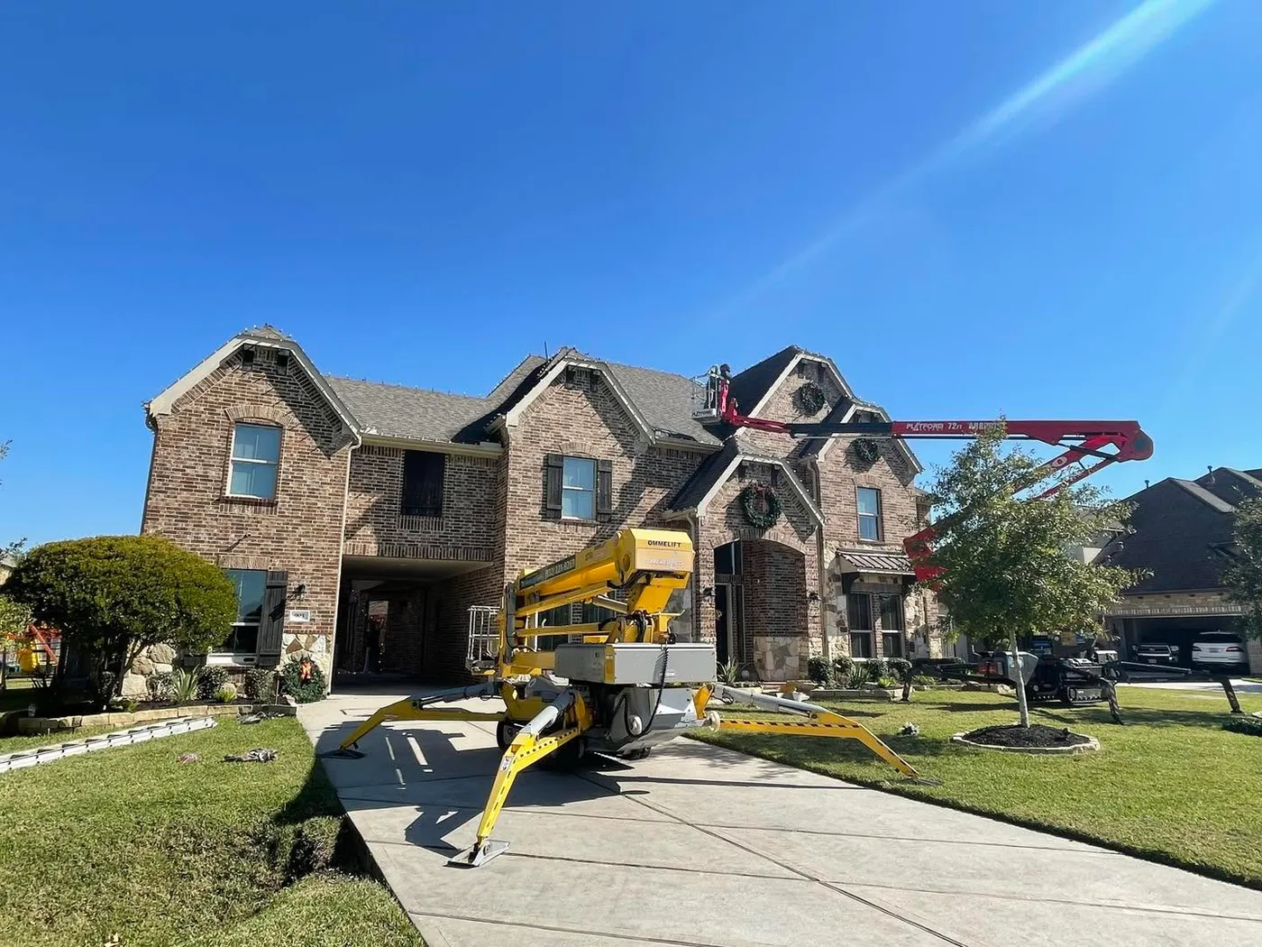 Installing Christmas lights on a two-story house with wreaths on all gables in process