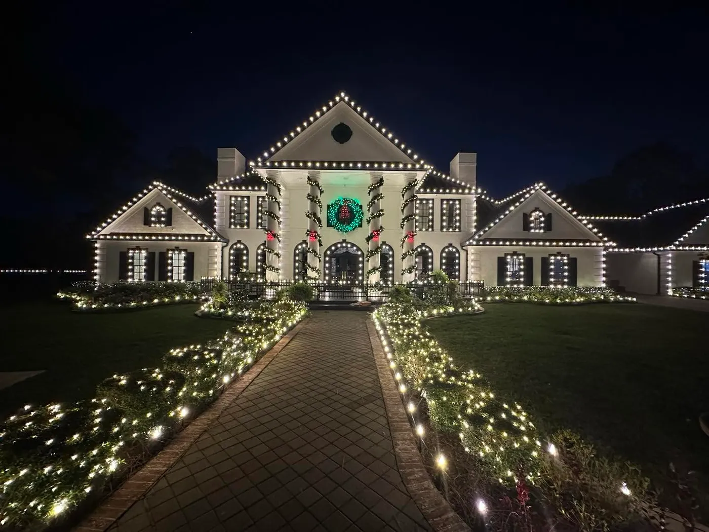 Palatial estate wrapped in Christmas lights, huge wreath above front door, pathway lined with Christmas lights