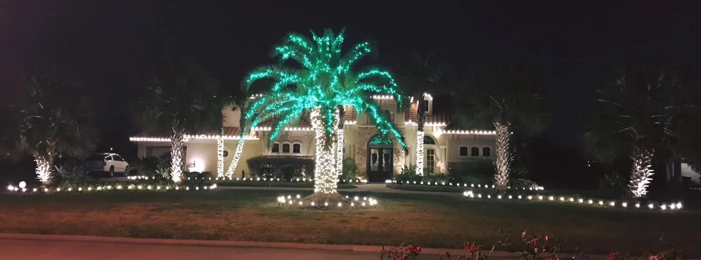 Caribbean or Spanish-style house with multiple palm trees wrapped with Christmas lights